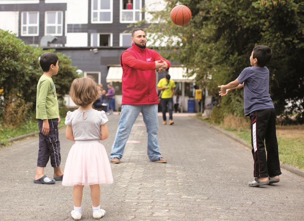 Ein Ehrenamtlicher spielt gemeinsam mit mehren Kindern mit einem Ball.