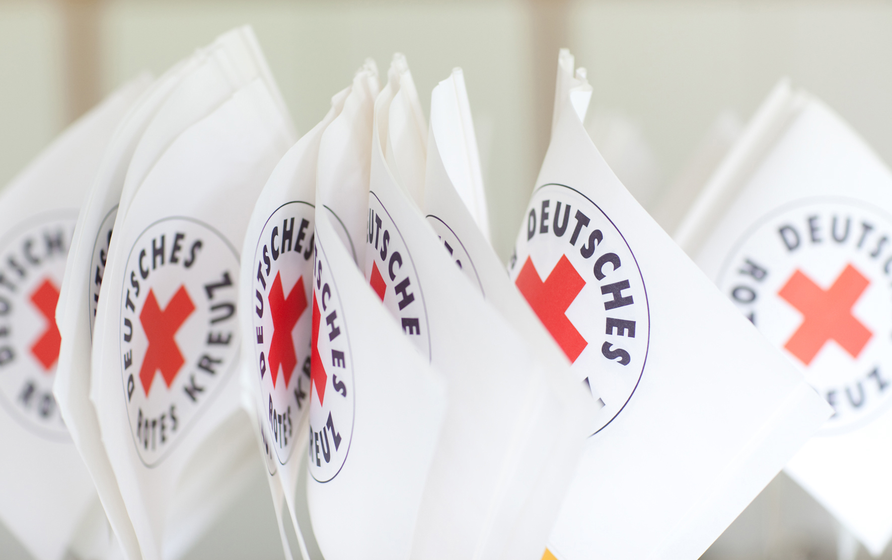 Mehrere Fähnchen mit dem Logo des Deutschen Roten Kreuzes sind nebeneinander zu sehen. 
