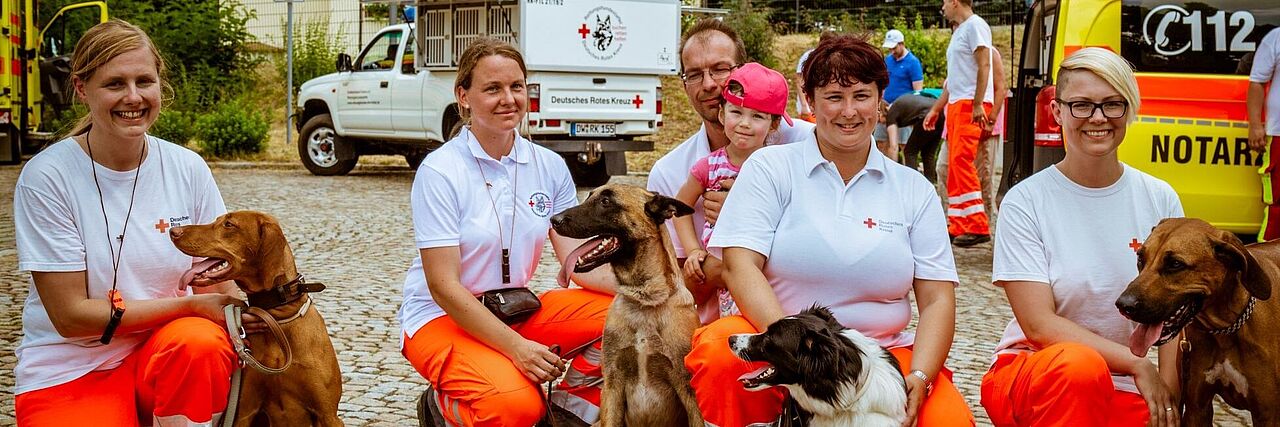 Fünf Ehrenamtliche der DRK Rettungshundestaffel hocken neben ihren Rettungshunden.