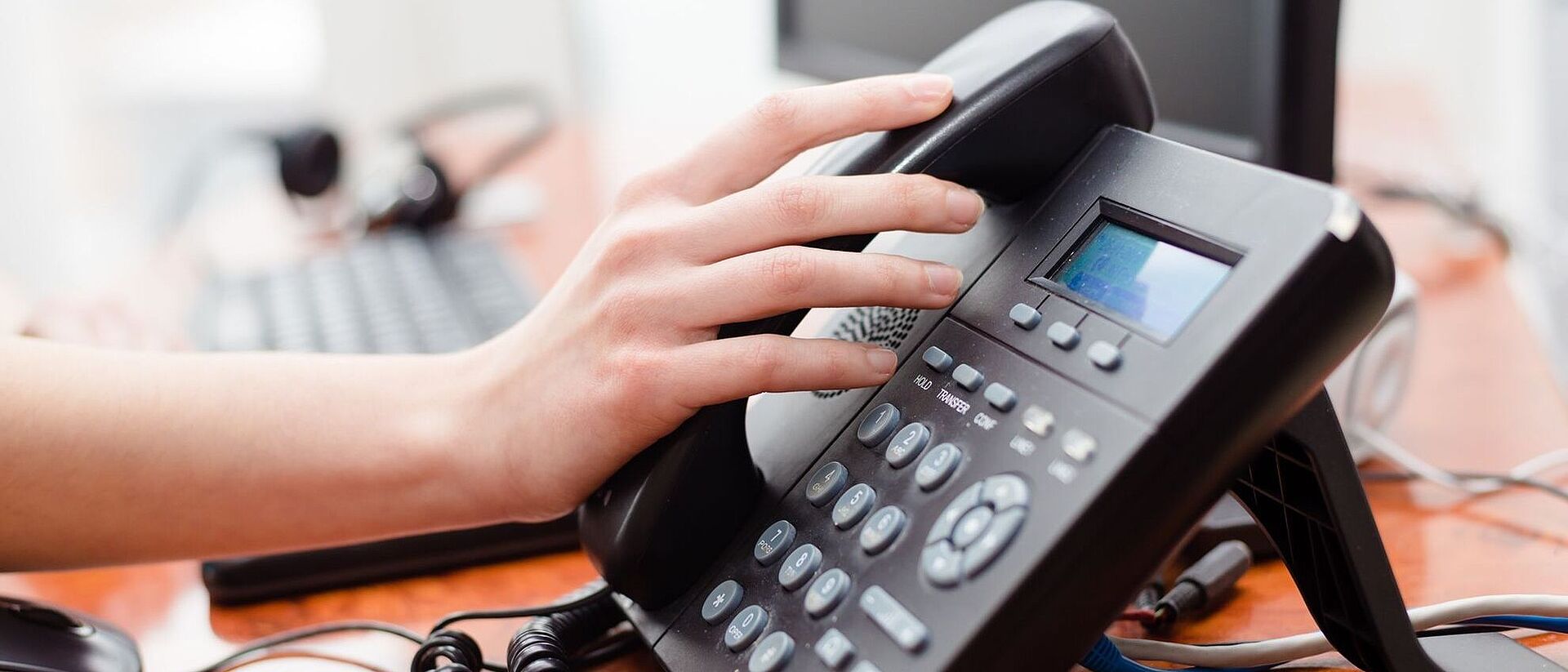 Ein Telefon ist zu sehen. Im Hintergrund sieht man einen Computer auf dem Schreibtisch stehen.