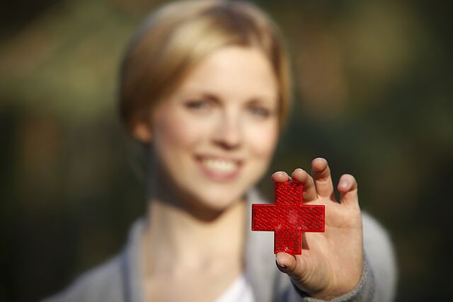 Eine Frau hält ihre ausgestreckte Hand in die Kamera. Darin hält sie ein reflektierendes Rotes Kreuz.
